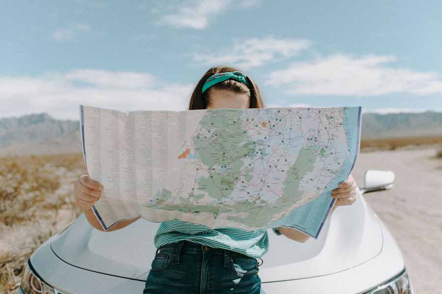 Girl holding a map sitting on her car